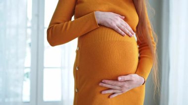 Hamilelik anneliği insanların gelecek beklentisi. Hamile kadın elleri pencerenin yanındaki koca göbeğe dokunuyor. Karnına sarılan ve hamileliğin tadını çıkaran bir kız. Annelik şefkati ebeveynlik yeni yaşam konsepti