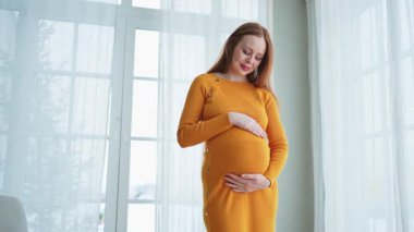 Hamilelik anneliği insanların gelecek beklentisi. Evinin penceresinin yanında koca göbekli hamile bir kadın var. Karnına sarılan ve hamileliğin tadını çıkaran bir kız. Annelik şefkati ebeveynlik yeni yaşam konsepti