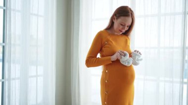 Hamilelik anneliği insanların gelecek beklentisi. Koca göbekli hamile bir kadın kucağında bebek poposu ile evde gülümsüyor. Genç anne hamileliğin tadını çıkarıyor. Annelik şefkati ebeveynlik yeni bir hayat