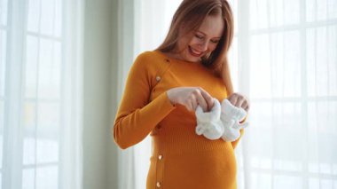 Hamilelik anneliği insanların gelecek beklentisi. Koca göbekli hamile bir kadın kucağında bebek poposu ile evde gülümsüyor. Genç anne hamileliğin tadını çıkarıyor. Annelik şefkati ebeveynlik yeni bir hayat