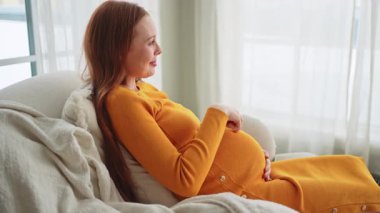 Hamilelik anneliği insanların gelecek beklentisi. Koca göbekli hamile bir kadın evdeki pencerenin yanındaki sandalyeye oturuyor. Karnına sarılan ve hamileliğin tadını çıkaran bir kız. Annelik şefkati ebeveynlik yeni bir hayat