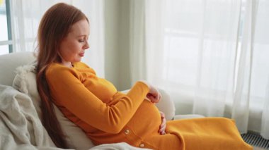 Hamilelik anneliği insanların gelecek beklentisi. Koca göbekli hamile bir kadın evdeki pencerenin yanındaki sandalyeye oturuyor. Karnına sarılan ve hamileliğin tadını çıkaran bir kız. Annelik şefkati ebeveynlik yeni bir hayat