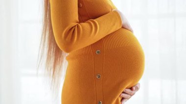 Hamilelik anneliği insanların gelecek beklentisi. Hamile kadın elleri pencerenin yanındaki koca göbeğe dokunuyor. Karnına sarılan ve hamileliğin tadını çıkaran bir kız. Annelik şefkati ebeveynlik yeni yaşam konsepti