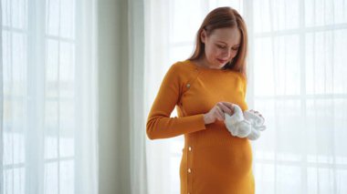 Hamilelik anneliği insanların gelecek beklentisi. Koca göbekli hamile bir kadın kucağında bebek poposu ile evde gülümsüyor. Genç anne hamileliğin tadını çıkarıyor. Annelik şefkati ebeveynlik yeni bir hayat