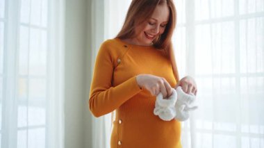 Hamilelik anneliği insanların gelecek beklentisi. Koca göbekli hamile bir kadın kucağında bebek poposu ile evde gülümsüyor. Genç anne hamileliğin tadını çıkarıyor. Annelik şefkati ebeveynlik yeni bir hayat