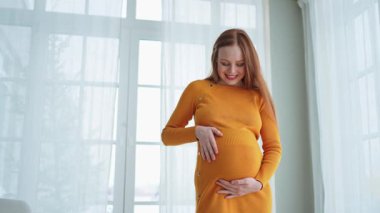 Hamilelik anneliği insanların gelecek beklentisi. Evinin penceresinin yanında koca göbekli hamile bir kadın var. Karnına sarılan ve hamileliğin tadını çıkaran bir kız. Annelik şefkati ebeveynlik yeni yaşam konsepti