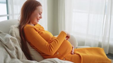 Hamilelik anneliği insanların gelecek beklentisi. Koca göbekli hamile bir kadın evdeki pencerenin yanındaki sandalyeye oturuyor. Karnına sarılan ve hamileliğin tadını çıkaran bir kız. Annelik şefkati ebeveynlik yeni bir hayat