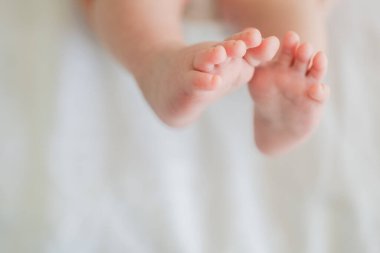 Minik bebek ayakları ve ayak parmakları beyaz arka planda. Beyaz battaniyenin altında yeni doğmuş bebek bacakları. Bebek yalınayak yaklaşın. Annelik şefkati ebeveynlik doğum günü. Mutlu Aile