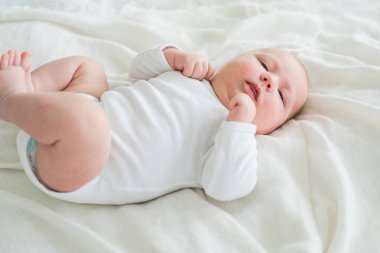 Mutlu bebek. Yatak odasında, gülümseyen yüzüyle küçük şirin bir kız. Bebek dinleniyor, evde beyaz battaniyeye uzanmış oynuyor. Annelik mutlu çocuk bakımı konsepti