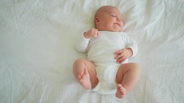Mutlu bebek. Yatak odasında, gülümseyen yüzüyle küçük şirin bir kız. Bebek dinleniyor, evde beyaz battaniyeye uzanmış oynuyor. Annelik mutlu çocuk bakımı konsepti
