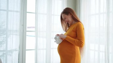 Hamilelik anneliği insanların gelecek beklentisi. Koca göbekli hamile bir kadın kucağında bebek poposu ile evde gülümsüyor. Genç anne hamileliğin tadını çıkarıyor. Annelik şefkati ebeveynlik yeni bir hayat