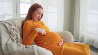 Hamilelik anneliği insanların gelecek beklentisi. Koca göbekli hamile bir kadın evdeki pencerenin yanındaki sandalyeye oturuyor. Karnına sarılan ve hamileliğin tadını çıkaran bir kız. Annelik şefkati ebeveynlik yeni bir hayat