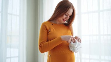 Hamilelik anneliği insanların gelecek beklentisi. Koca göbekli hamile bir kadın kucağında bebek poposu ile evde gülümsüyor. Genç anne hamileliğin tadını çıkarıyor. Annelik şefkati ebeveynlik yeni bir hayat