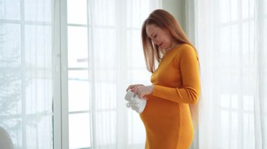 Hamilelik anneliği insanların gelecek beklentisi. Koca göbekli hamile bir kadın kucağında bebek poposu ile evde gülümsüyor. Genç anne hamileliğin tadını çıkarıyor. Annelik şefkati ebeveynlik yeni bir hayat