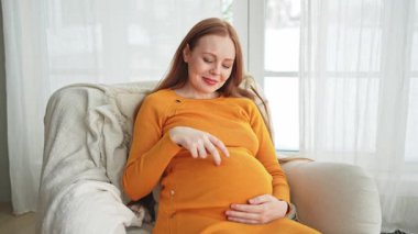 Hamilelik anneliği insanların gelecek beklentisi. Koca göbekli hamile bir kadın evdeki pencerenin yanındaki sandalyeye oturuyor. Karnına sarılan ve hamileliğin tadını çıkaran bir kız. Annelik şefkati ebeveynlik yeni bir hayat