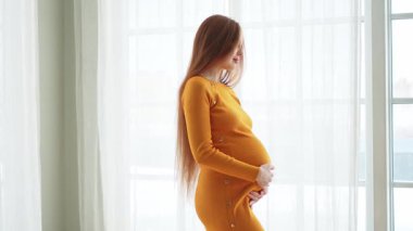 Hamilelik anneliği insanların gelecek beklentisi. Evinin penceresinin yanında koca göbekli hamile bir kadın var. Karnına sarılan ve hamileliğin tadını çıkaran bir kız. Annelik şefkati ebeveynlik yeni yaşam konsepti