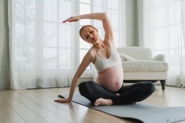 Hamilelik yoga antrenmanı. Hamile kadın evde yoga yapıyor. Hamile kız içeride yoga minderiyle spor yapıyor. Koca göbekli bir kadın Asya antrenmanı yapıyor.