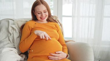 Hamilelik anneliği insanların gelecek beklentisi. Koca göbekli hamile bir kadın evdeki pencerenin yanındaki sandalyeye oturuyor. Karnına sarılan ve hamileliğin tadını çıkaran bir kız. Annelik şefkati ebeveynlik yeni bir hayat