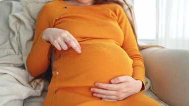 Hamilelik anneliği insanların gelecek beklentisi. Hamile kadın elleri pencerenin yanındaki koca göbeğe dokunuyor. Karnına sarılan ve hamileliğin tadını çıkaran bir kız. Annelik şefkati ebeveynlik yeni yaşam konsepti