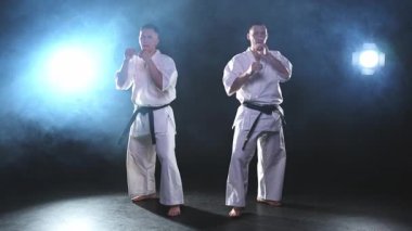 Karanlık arka planda dövüş sanatları ustaları. Siyah spor salonunda karate dövüş sporları eğitimi için beyaz kimonolu güçlü dövüşçüler. Karate dövüşçüleri antrenman yapıyor. Dövüş antrenmanı yapıyor.
