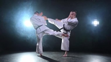 Karanlık arka planda dövüş sanatları ustaları. Siyah spor salonunda karate dövüş sporları eğitimi için beyaz kimonolu güçlü dövüşçüler. Karate dövüşçüleri antrenman yapıyor. Dövüş antrenmanı yapıyor.