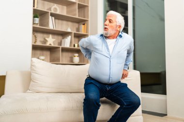 Sırt ağrısı. Memnuniyetsiz yaşlı adam evde sırt ağrısı çekiyor. Yaşlı adam aniden sırt ağrısı hisseder kaslar gerilim yaralanması. Üzgün büyükbaba sırtı ağrıyan omurgaya dokunuyor.