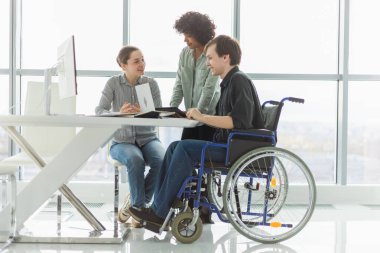 Takım çalışması beyin fırtınası. Çeşitli çok ırklı meslektaşlar birlikte çalışan engelli insanlar için sandalyede oturuyor. Yaratıcı ofiste oturup iş konuşan bir grup insan. Genç profesyonel takım