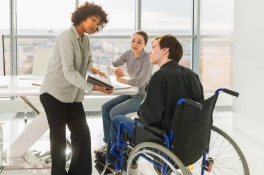 Takım çalışması beyin fırtınası. Çeşitli çok ırklı meslektaşlar birlikte çalışan engelli insanlar için sandalyede oturuyor. Yaratıcı ofiste oturup iş konuşan bir grup insan. Genç profesyonel takım