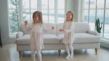 Mutlu aile kardeş sevgisi. İki komik ikiz kız kardeş dans ederek evde birlikte oynuyorlar. Mutlu çocuk yaşam tarzı. Oyun oynayan tek yumurta ikizi kızlar. Kızlar arkadaşlık ve gençlik