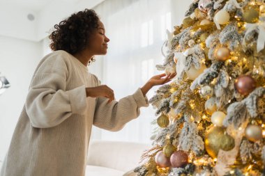 Mutlu noeller. Noel ağacı süsleyen Afrikalı Amerikalı kadın. Klasik Noel ağacının yanında beyaz gümüş süslemeleri olan mutlu bir kız. Noel arifesinde evde kutlama zamanı.