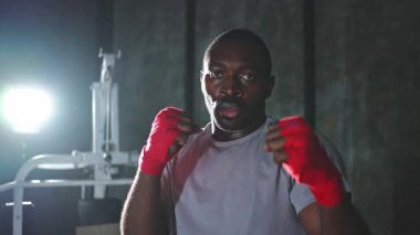 Spor salonunda boksör. Saldırgan Afrikalı dövüşçü boks eğitiminden sonra dinleniyor kameraya bakarak dövüşmeye hazır. Güçlü terli adam yumruklarını eğitiyor. Doğruca antrenmana hazırlanıyor.