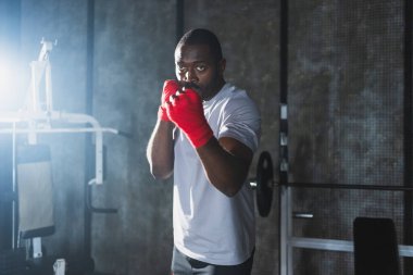 Beden eğitiminde. Afrikalı dövüşçü boksörlere yumruk atmaya hazır koruyucu bandajları kameraya sarar. Güçlü bir adam boks antrenmanına hazırlanıyor.