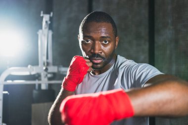 Beden eğitiminde. Afrikalı dövüşçü boksörlere yumruk atmaya hazır koruyucu bandajları kameraya sarar. Güçlü bir adam boks antrenmanına hazırlanıyor.
