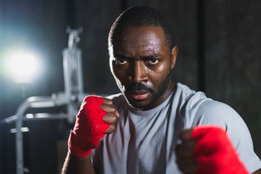 Spor salonunda boksör. Saldırgan Afrikalı dövüşçü boks eğitiminden sonra dinleniyor kameraya bakarak dövüşmeye hazır. Güçlü terli adam yumruklarını eğitiyor. Doğruca antrenmana hazırlanıyor.