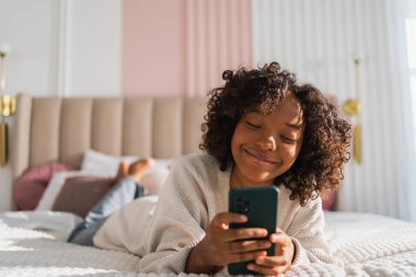 African girl holding smartphone touch screen typing scroll page at home. Woman with cell phone surfing internet using social media apps playing game. Shopping online Internet news cellphone addiction