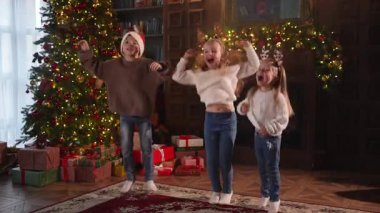 Mutlu Noeller Noel tatili. Çocuklar dans edip zıplayarak Noel ağacının yanında eğleniyorlar. Mutlu çocuklar oturma odasında Noel ağacı ve şömineyle gülüyorlar. Evde Noel arifesi