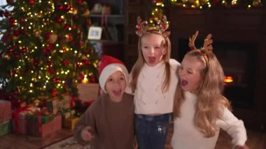 Mutlu Noeller Noel tatili. Çocuklar dans edip zıplayarak Noel ağacının yanında eğleniyorlar. Mutlu çocuklar oturma odasında Noel ağacı ve şömineyle gülüyorlar. Evde Noel arifesi