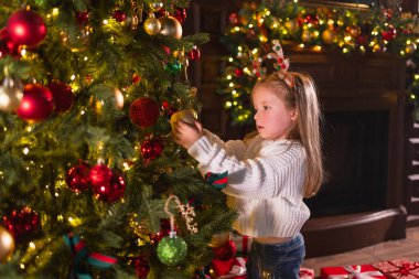 Mutlu Noeller Noel tatili. Noel arifesinde evde Noel ağacı süsleyen küçük bir kız. Klasik Noel ağacının yanında, elinde kış süsleri olan genç bir çocuk. Kutlama zamanı.