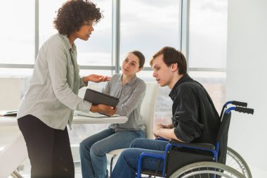 Takım çalışması beyin fırtınası. Çeşitli çok ırklı meslektaşlar birlikte çalışan engelli insanlar için sandalyede oturuyor. Yaratıcı ofiste oturup iş konuşan bir grup insan. Genç profesyonel takım