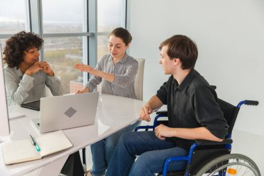 Takım çalışması beyin fırtınası. Çeşitli çok ırklı meslektaşlar birlikte çalışan engelli insanlar için sandalyede oturuyor. Yaratıcı ofiste oturup iş konuşan bir grup insan. Genç profesyonel takım