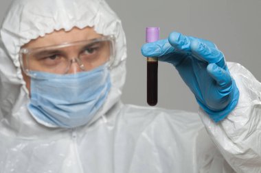 Scientific virologist. Biologist in protective suit and blue gloves holds test tube with blood. Test tube with viruses concept. Virus University employee.