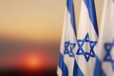 Israel flags with a star of David over cloudy sky background on sunset. Patriotic concept about Israel with national state symbols. Banner with place for text.