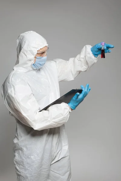 Scientific virologist. Biologist in protective suit and blue gloves holds test tubes with blood. Test tube with viruses concept. Virus University employee.