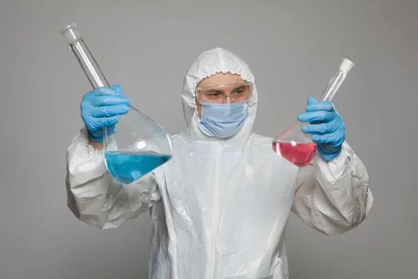 Scientific virologist. Biologist in protective suit and blue gloves holds big flasks with substance samples. Flasks with viruses concept. Virus University employee.
