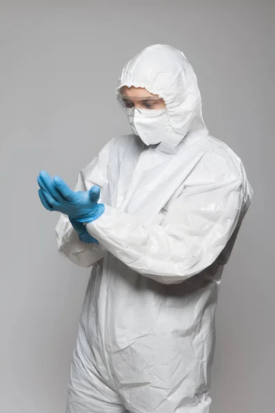 Scientific virologist. Biologist in protective suit and goggles putting on blue gloves. Viruses concept. Virus University employee.