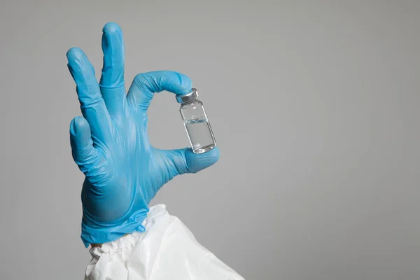 Closeup of vial to vaccinate in scientific virologist hand for immunization. Scientific virologist. Biologist in protective suit and blue gloves. Vaccination concept.