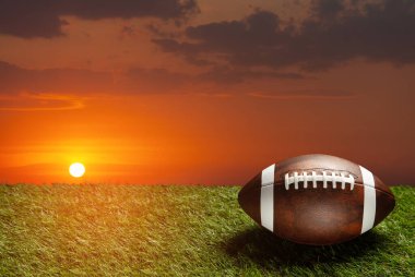 American football ball on green grass field on background of sunset sky. Banner with space for text.