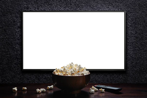 Television on a dark gray wall with remote control and popcorn bowl on the table. TV 4K flat screen lcd or oled, White blank HD monitor mockup. Modern video panel black flatscreen.