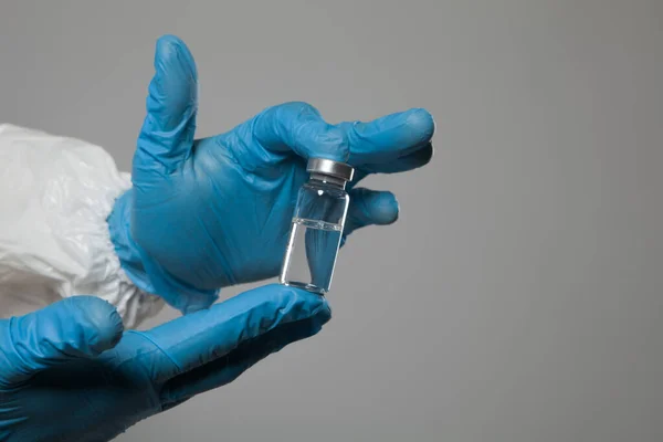 Closeup of vial to vaccinate in scientific virologist hand for immunization. Scientific virologist. Biologist in protective suit and blue gloves. Vaccination concept.
