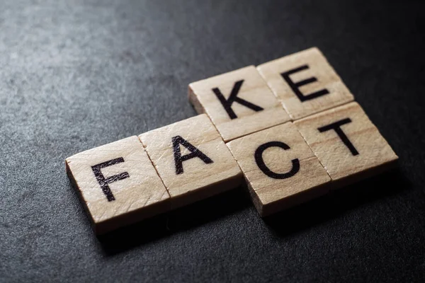 Wooden blocks forming words Fact and Fake on black background.